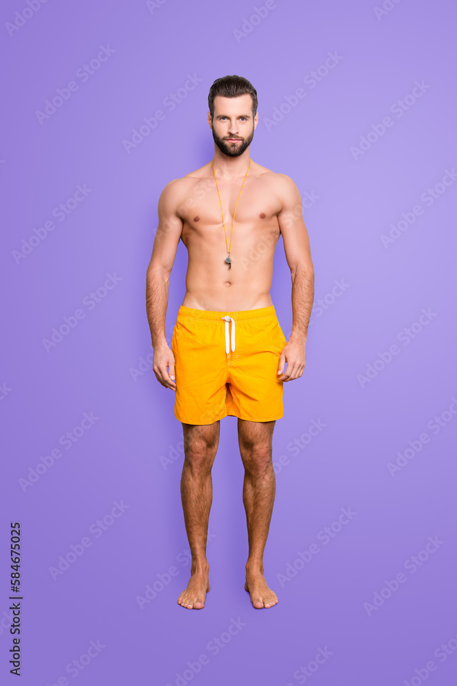 Full size body portrait of fit sportive lifeguard with stubble in yellow shorts isolated over grey background, looking at camera