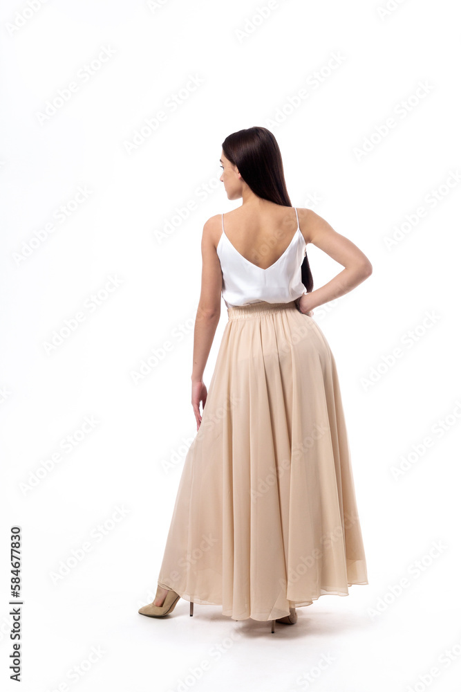 Young woman with dark hair in a white top posing on a white background with her back