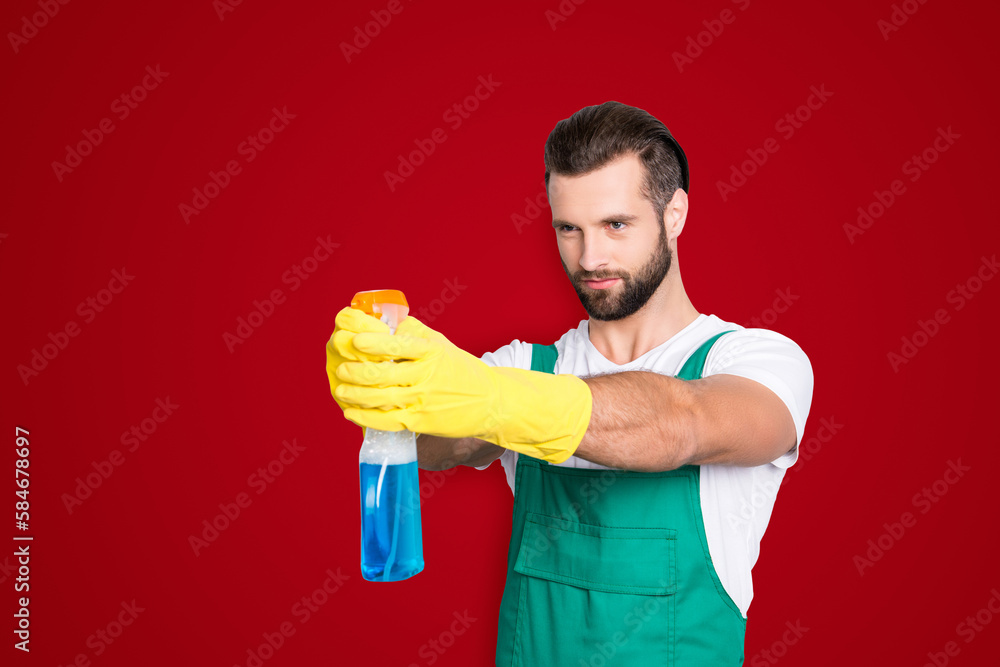 Portrait of funny comic cleaner in uniform t-shirt overall with stubble holding detergent spray with blue liquid like gun, isolated on grey background Portrait of funny comic cleaner in uniform t-shirt overall with stubble holding detergent spray with blue liquid like gun, isolated on grey background