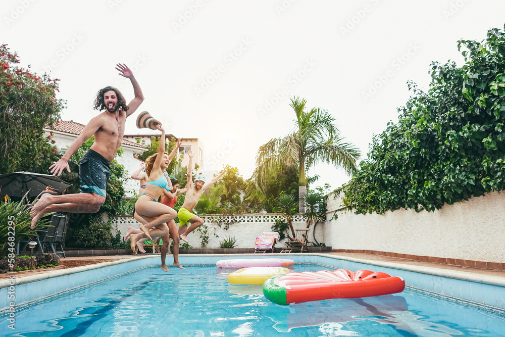Group of happy friends jumping inside pool during summer vacations - Soft focus on left girl face - Summer, party and travel concept