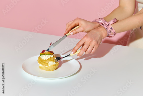 Cropped shot of model female bound hands with measuring tape taking cake over pink background. Close-up