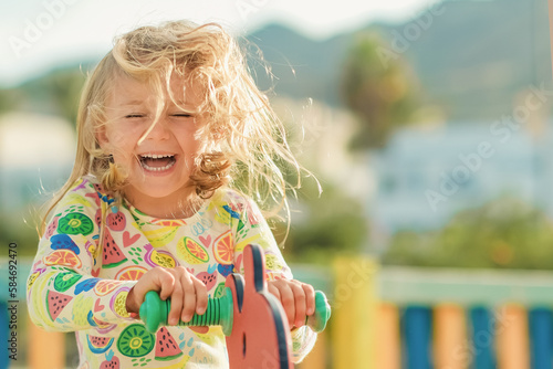 sunny summer day excited happy smiling face child girl in yellow dress play on colored wooden children playground in kindergarten