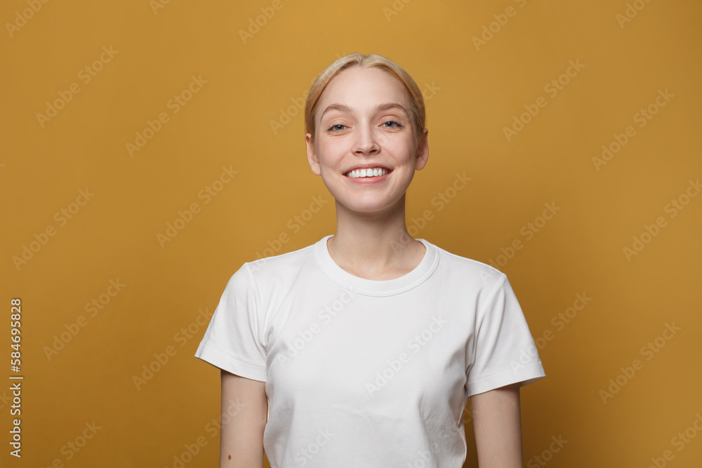 Happy cute woman wearing white empty t-shirt smiling on vivid yellow studio background Happy cute woman wearing white empty t-shirt smiling on vivid yellow studio background