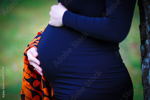 A pregnant woman wearing a blue dress holds her stomach with both hands