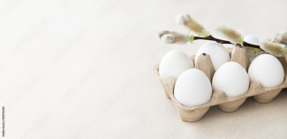 Easter holiday. White eggs in an eco box - a willow branch on top, background - natural linen fabric. 