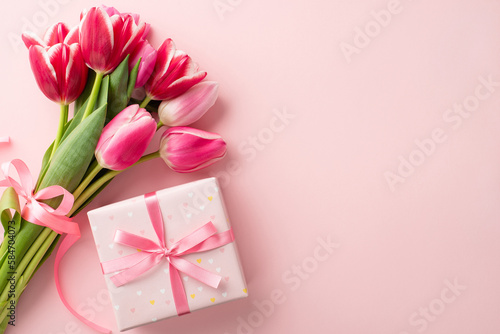 Mother's Day celebration concept. Top view photo of giftbox with ribbon bow and bouquet of pink tulips on isolated pastel pink background with copyspace © ActionGP