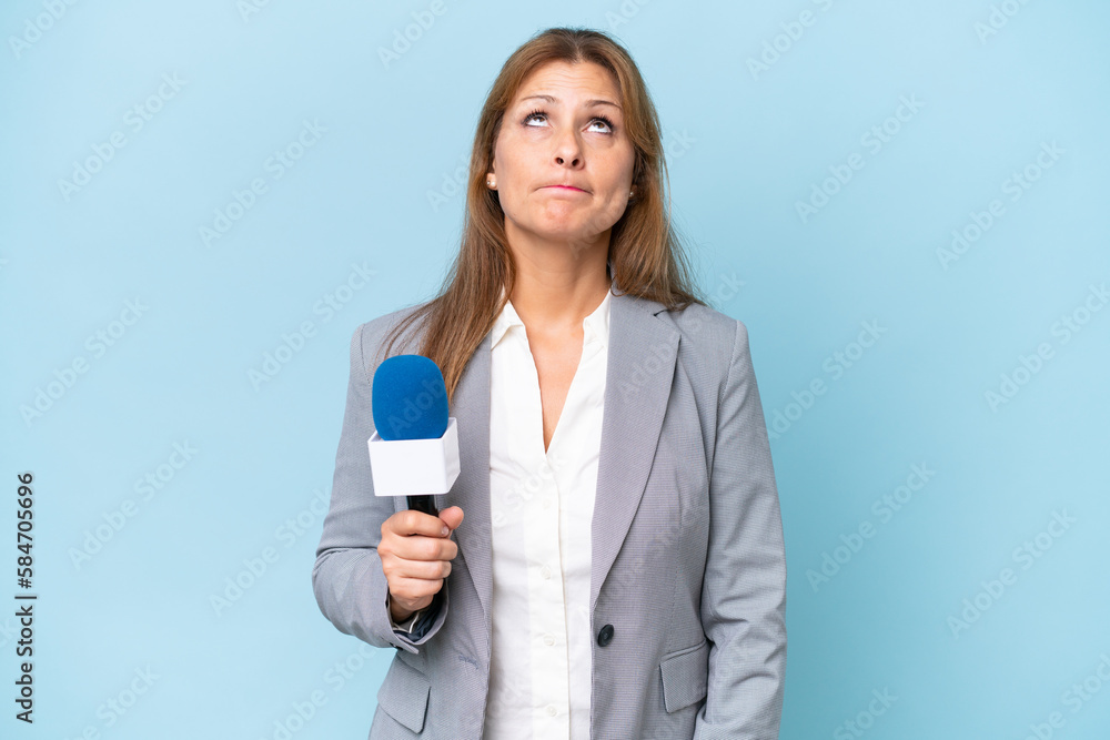 Middle-aged TV presenter woman over isolated blue background and looking up Middle-aged TV presenter woman over isolated blue background and looking up