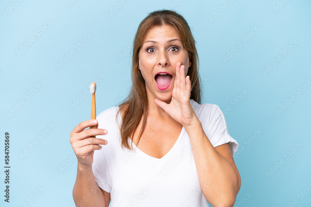 Middle-aged caucasian woman brushing teeth isolated on blue background shouting with mouth wide open Middle-aged caucasian woman brushing teeth isolated on blue background shouting with mouth wide open