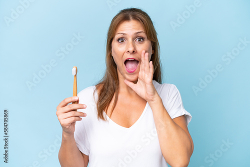 Middle-aged caucasian woman brushing teeth isolated on blue background shouting with mouth wide open