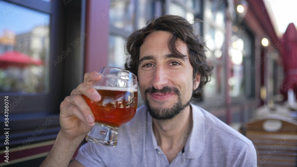 Portrait of a 30s young man holding draft beer seated at outdoors restaurant. Pale ale alcoholic drink