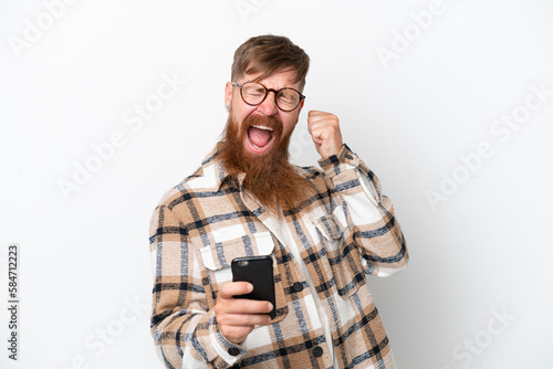 Redhead man with long beard isolated on white background with phone in victory position