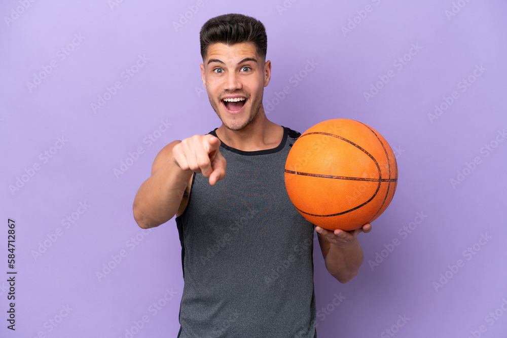 young caucasian woman  basketball player man isolated on purple background surprised and pointing front