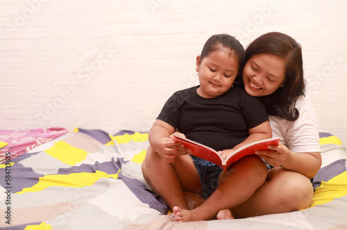 Mother and daughter reading a book on the bed at home
