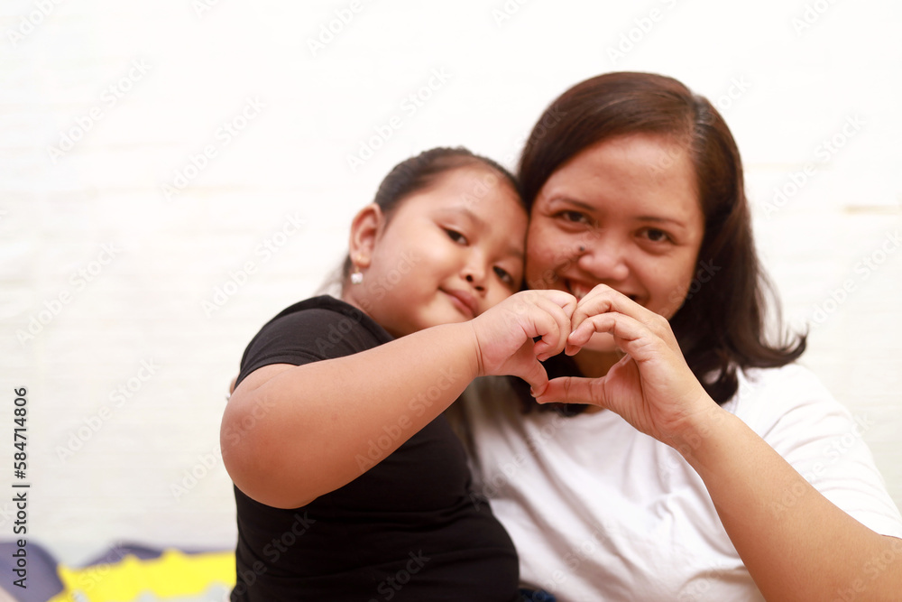Happy mom and his daughter making love hand shape on the bed at home Happy mom and his daughter making love hand shape on the bed at home