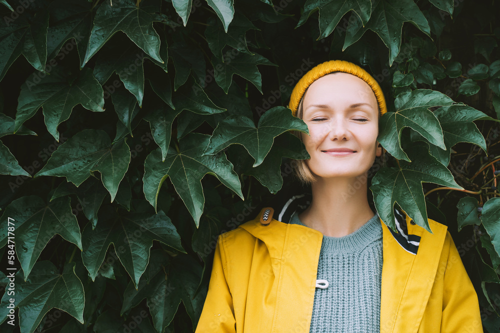 Portrait of relaxed and confident woman with eyes closed on background of green leaves wall. Thoughtful person in front of green hedge. Joy, zen and balance people. Stability through mental health - obrazy, fototapety, plakaty 