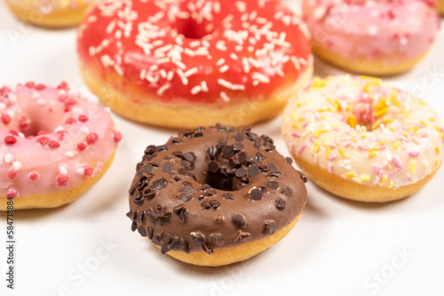 Many different donuts on a white background top view, pink, white and chocolate donuts of different sizes