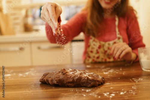 Image of hand sprinkling flour on dough. Close-up of woman sprinkling flour on the dough she kneaded in the kitchen.