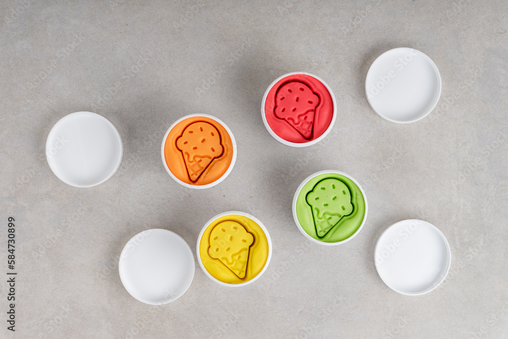 Colorful dough in white jars on gray background. Flat lay