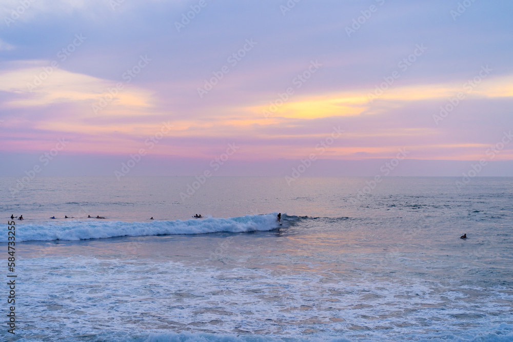 Obraz premium Surfers catch waves, surfing at sunset. Bali.