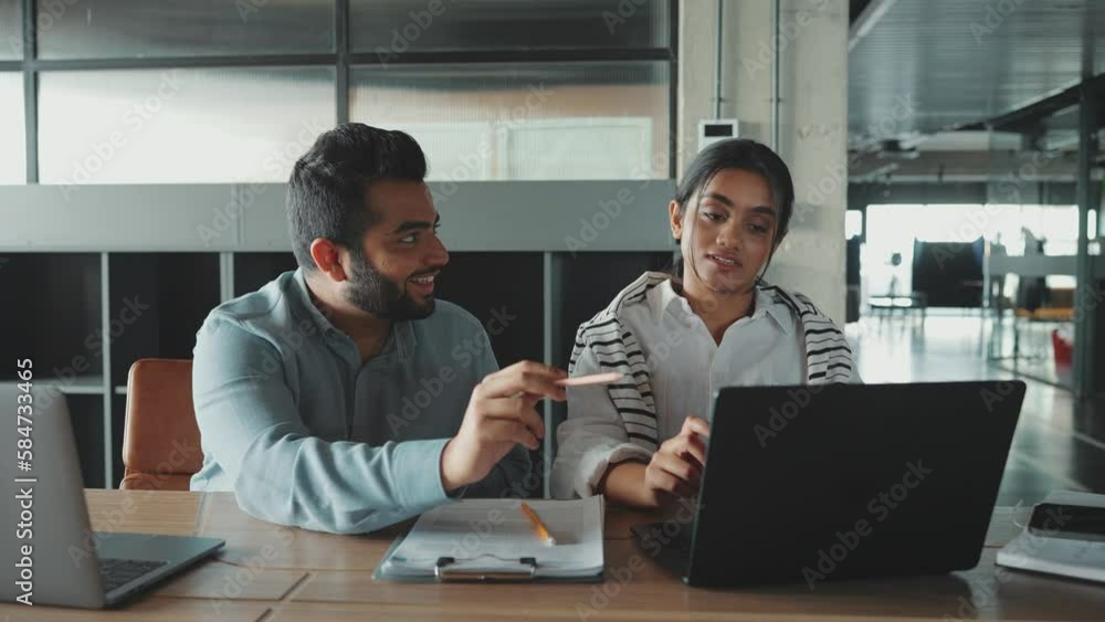 Smiling Indian colleagues discuss laptop work in a co-working room Smiling Indian colleagues discuss laptop work in a co-working room