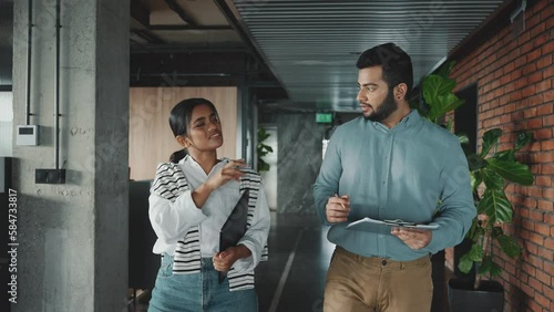 Confident Indian colleagues discussing work while walking in the office