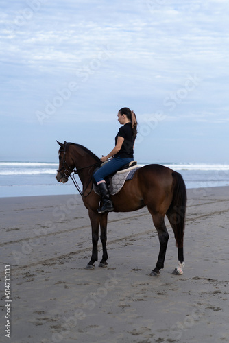 Young woman riding a horse on the beach at the ocean. © Yuliya Kirayonak