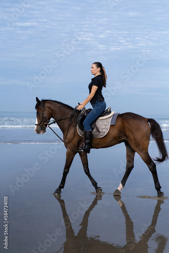 Young woman riding a horse on the beach at the ocean.