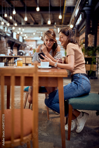 Young happy girlfriends enjoying coffee time together. Modern industrial cafe interior background.