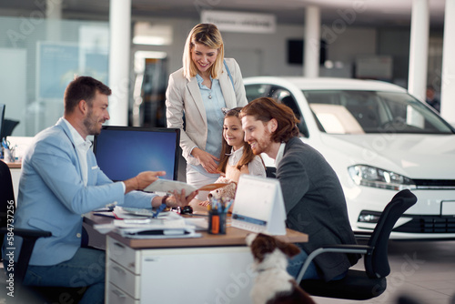 Happy family in car selling salon with salesman