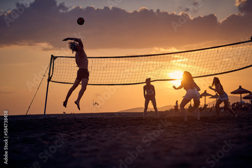 A group of friends is playing the volleyball on the beach while sun is setting. Sport, sea, beach