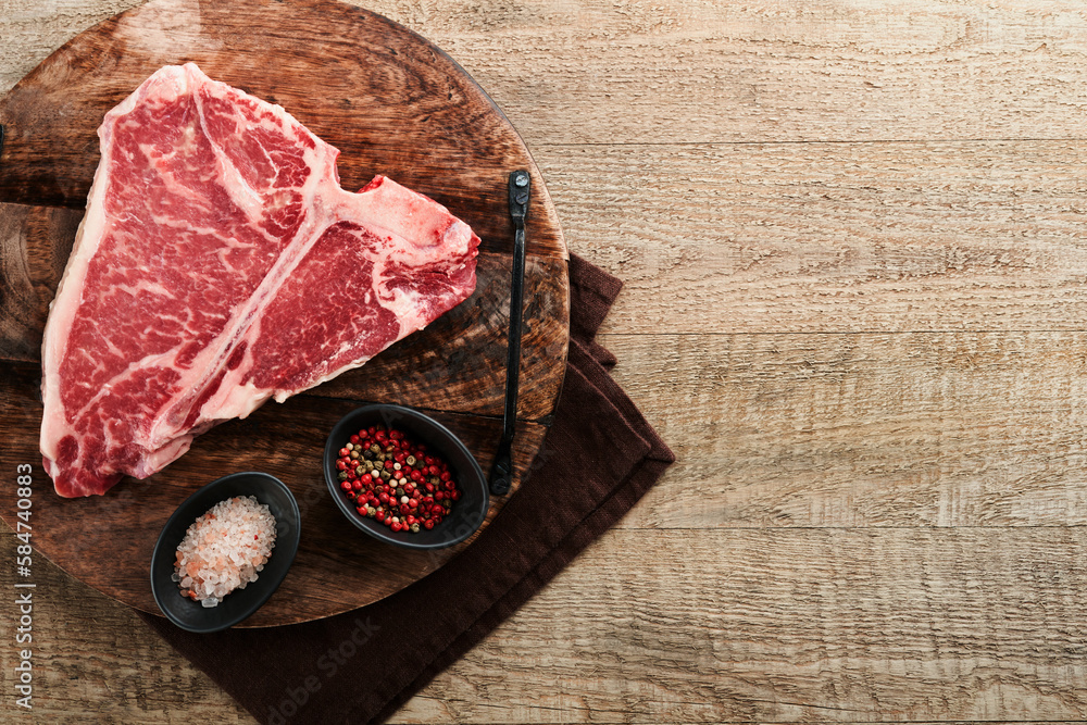 Thick Raw T-Bone Steak. Dry-aged Raw T-bone or porterhouse beef meat Steak on cutting boar with herbs and salt on dark background. Top view and copy space.