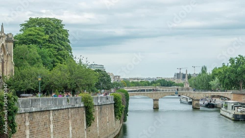 Notre Dame de Paris Garden on Cite Island timelapse, Paris, France. Park with green trees and flowers. View from Double bridge. River with floating boats. Cloudy sky at summer day photo