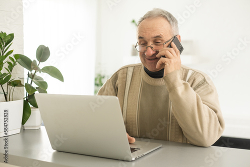 senior man looking at laptop and phone calling at home. photo
