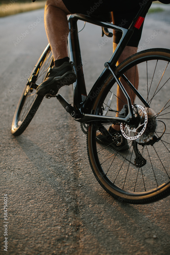 Close-up photo of a man dressed in cycling clothes starting riding a modern bicycle on the asphalt out-of-town bicycle path. Active sporty people concept image Close-up photo of a man dressed in cycling clothes starting riding a modern bicycle on the asphalt out-of-town bicycle path. Active sporty people concept image