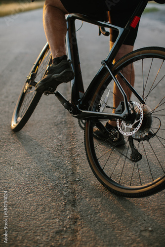 Close-up photo of a man dressed in cycling clothes starting riding a modern bicycle on the asphalt out-of-town bicycle path. Active sporty people concept image