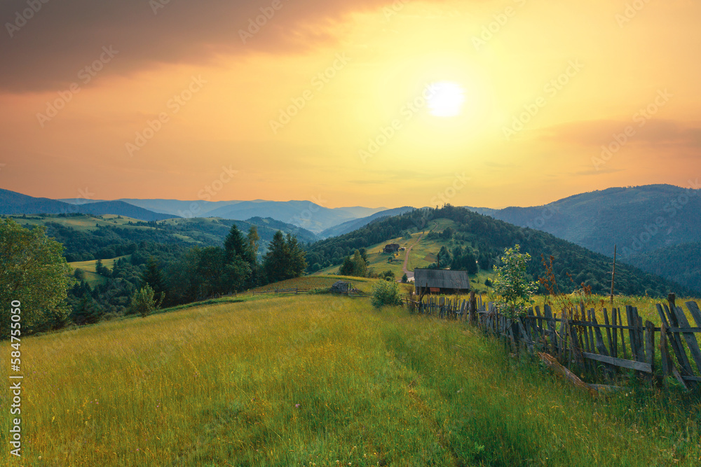 Idyllic rural scenery in the Carpathian mountains, Ukraine. Old wooden fence goes along the pathway on the high grass hill under the bright sunset sky.
