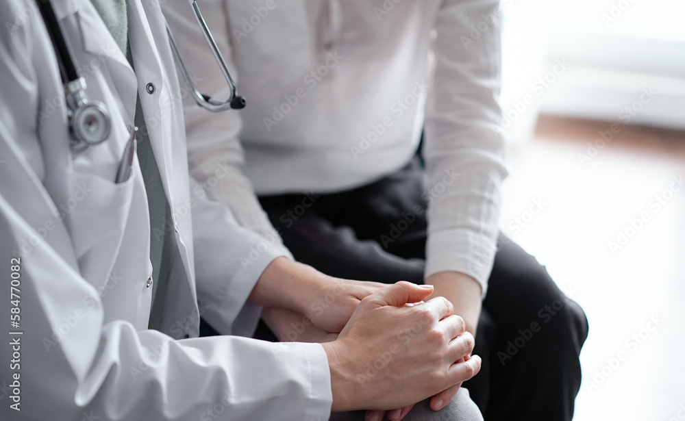 Doctor and patient sitting at sofa. The focus is on female physician's hands reassuring woman, close up. Medicine concept