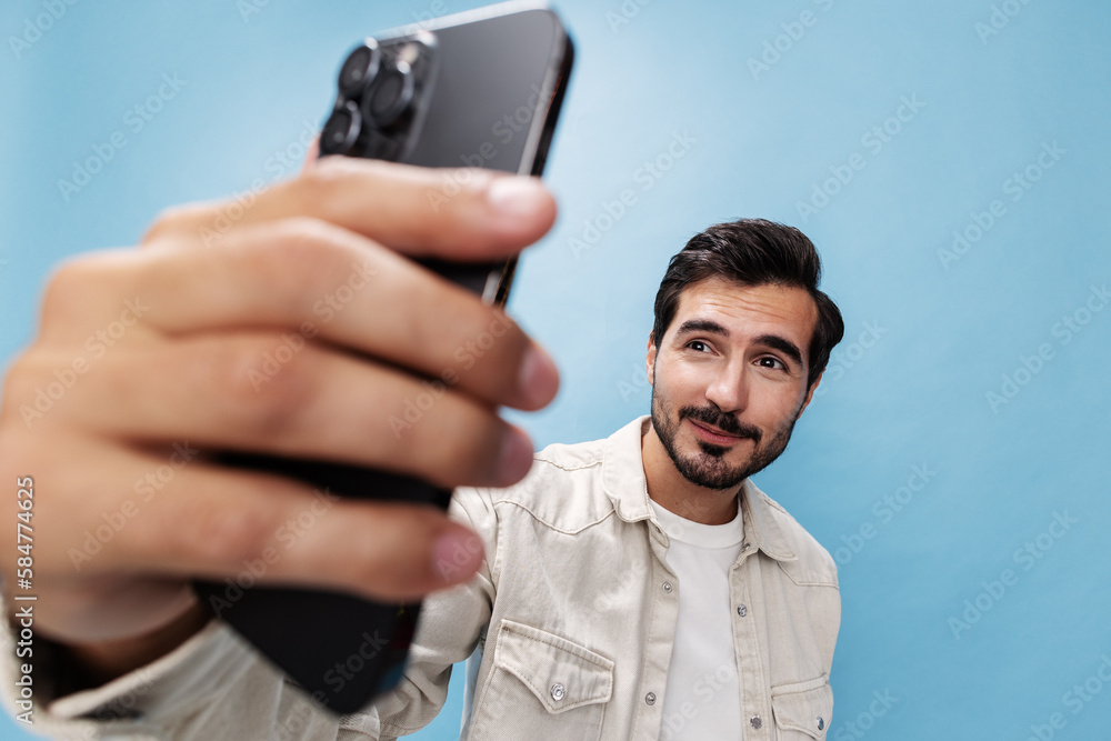 Portrait of a man brunette smile looking at the phone blogger with a beard taking selfies, on a blue background in a white T-shirt and jeans, copy space Portrait of a man brunette smile looking at the phone blogger with a beard taking selfies, on a blue background in a white T-shirt and jeans, copy space