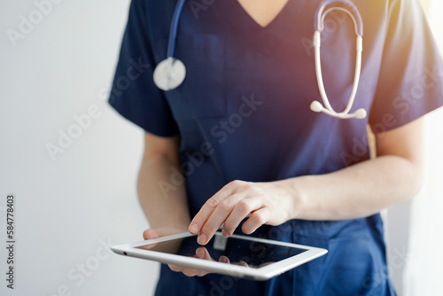 Doctor woman using tablet computer while standing near panorama window in clinic, close up. Physician or surgeon at work. Medicine concept photo