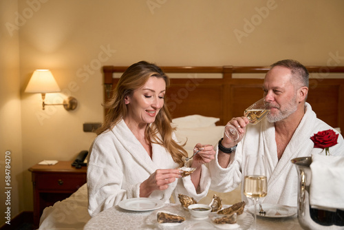 Couple in bathrobes enjoys oysters and champagne in luxury hotel room