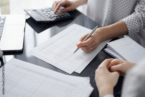 Woman accountant using a calculator and laptop computer while counting taxes for a client. Business audit and finance concepts