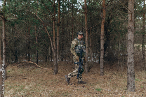 a soldier walks through the forest with a machine gun. military in full-length camouflage