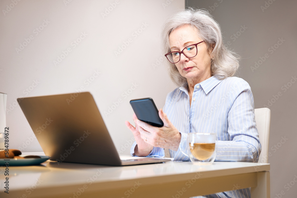 Serious lady with glasses settled down with laptop at kitchen table Serious lady with glasses settled down with laptop at kitchen table