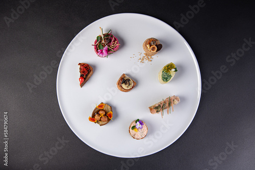 top view on various gastronomic appetizer on a white plate isolated on a black background