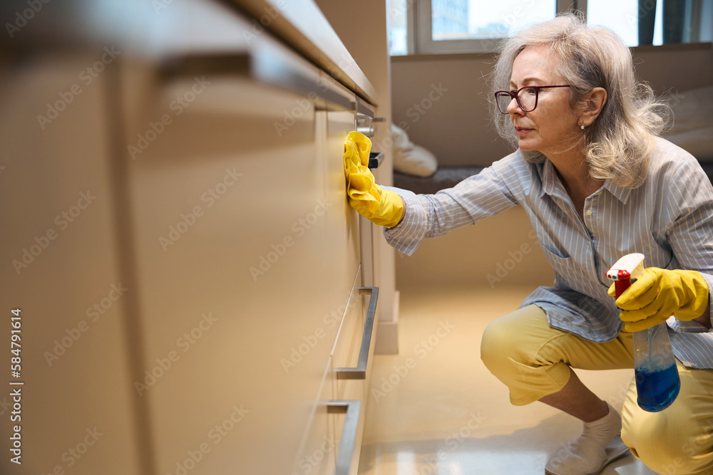 Cute slender grandmother washes kitchen surfaces squatting Cute slender grandmother washes kitchen surfaces squatting