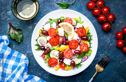 Greek salad with feta cheese, kalamata olives, red tomato, yellow paprika, cucumber and onion, healthy mediterranean diet food, low calories eating. Blue stone background, top view