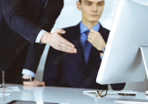 Two businessmen discussing questions at meeting in a modern office, using a computer. Headshot at negotiation or workplace. Teamwork, partnership and business concept