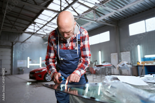 Male worker in a repair shop works with a windshield
