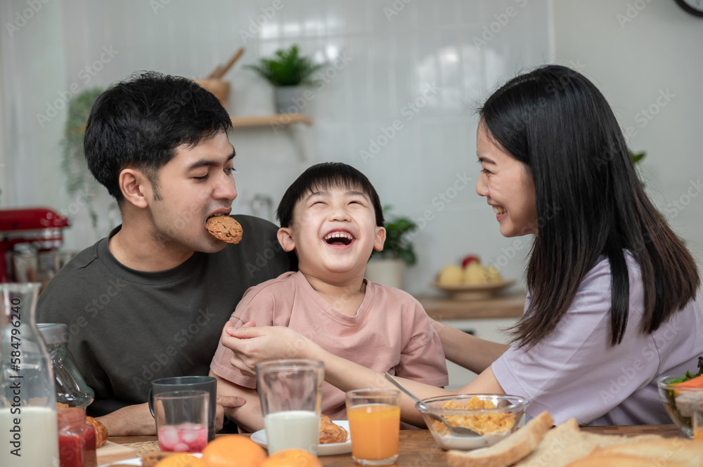 Happy Asian family enjoying breakfast together on dinning table. Young Asian father taking a glass of milk to his son while having breakfast in the kitchen. Happy Asian family lifestyle concept. Happy Asian family enjoying breakfast together on dinning table. Young Asian father taking a glass of milk to his son while having breakfast in the kitchen. Happy Asian family lifestyle concept.