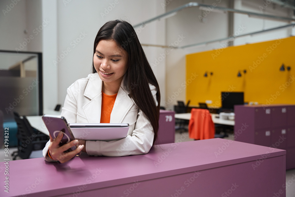 Joyous corporate worker reading something on cellphone in open-place office Joyous corporate worker reading something on cellphone in open-place office